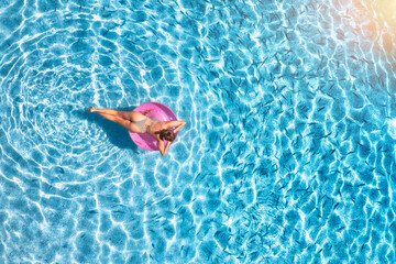 Aerial view of a young woman swimming with pink swim ring in blue sea with school of fish at sunset...
