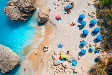 Aerial view of blue sea, sandy beach with umbrellas, stones and rocks in water at sunset in summer....
