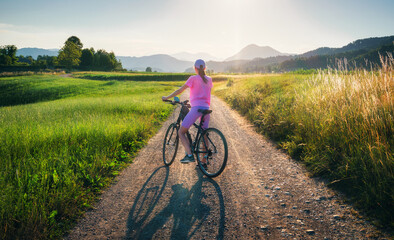 Woman on mountain bike on gravel road at sunset in summer. Colorful landscape with sporty girl...