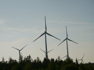 Group of wind turbines are in the sky, with the sun setting behind them
