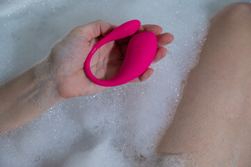 A woman lies in a bubble bath and holds a curved pink vibrator.