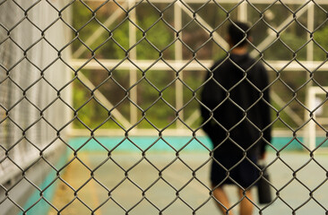 Focused metal mesh with young sportsman holding a water bottle out of focus in the background in a...