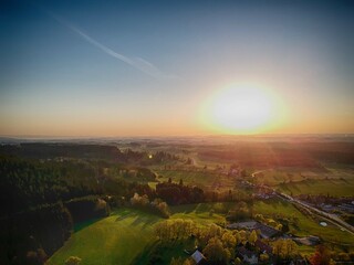 The sun is setting over a rural landscape, casting a warm glow over the fields