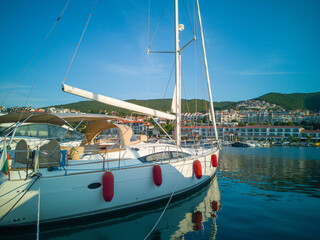 Two sailboats are moored at a marina, with clear blue skies and green hills in the background,...