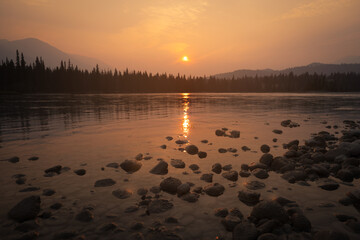 View of the sun reflecting off the water with rocks in the foreground and mountains in the background, Jasper National Park, Alberta, Canada.