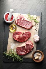 Pieces of raw beef meat and spices on black table, flat lay