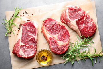 Pieces of raw beef meat and spices on grey table, flat lay