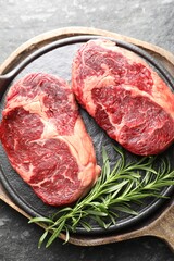 Pieces of raw beef meat and rosemary on dark table, top view