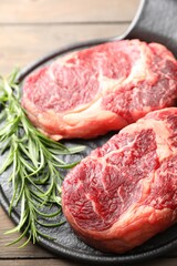 Pieces of raw beef meat and rosemary on table, closeup