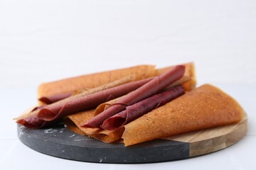 Delicious fruit leather rolls on white table, closeup