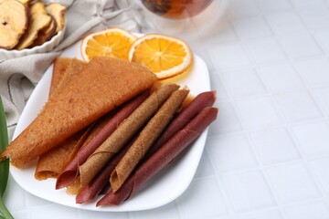 Tasty fruit leather rolls and orange slices on white table, closeup