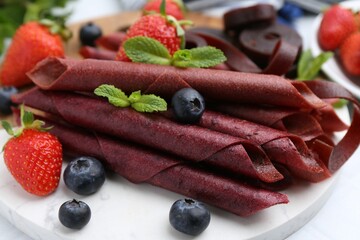 Tasty fruit leather rolls, strawberries, blueberries and mint on white table, closeup