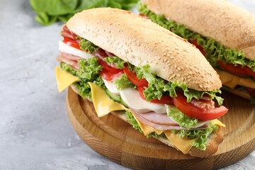 Tasty baguette sandwiches with ham, cheese and vegetables on grey textured table, closeup