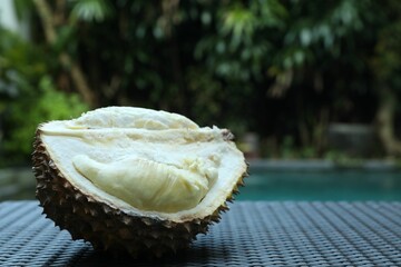 Fresh ripe durian on wicker table near swimming pool outdoors, closeup. Space for text