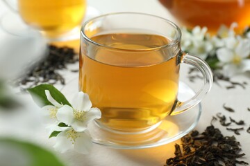 Aromatic jasmine tea in glass cup, flowers and dried leaves on white table, closeup