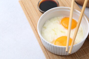 Traditional asian breakfast with half-boiled eggs in bowl, soy sauce and chopsticks on light grey table, closeup. Space for text