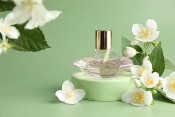 Bottle of perfume and jasmine flowers on green background, closeup