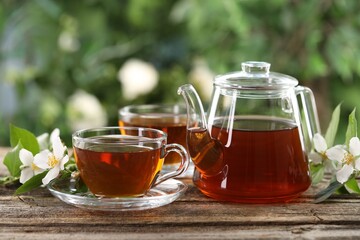 Tasty jasmine tea in cups, teapot and flowers on wooden table, closeup