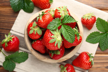 Fresh ripe strawberries and leaves in bowl on wooden table, flat lay