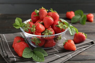 Fresh ripe strawberries and leaves in container on black wooden table, closeup