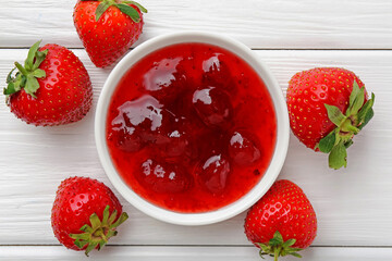 Tasty strawberry jam in bowl and fresh berries on white wooden table, flat lay