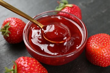 Taking tasty homemade strawberry jam with spoon at black table, closeup