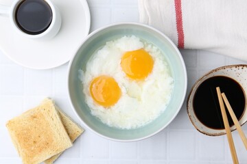 Traditional asian breakfast with half-boiled eggs in bowl, soy sauce, bread, chopsticks and coffee on white tiled table, flat lay