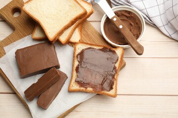 Tasty chocolate butter, slices of bread and knife on light wooden table, flat lay