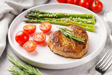 Close up, macro of tasty grilled beef steak served with green asparagus and cherry tomatoes on white plate, with cutlery. Perfect for food menu, diet, or culinary design concepts.