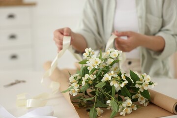 Woman making bouquet of jasmine branches at white table, closeup