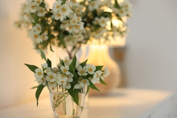 Bouquet of beautiful jasmine flowers in vase on white table indoors, closeup. Space for text