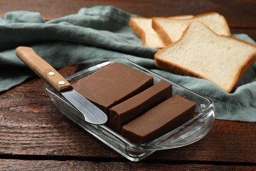 Tasty chocolate butter, slices of bread and knife on wooden table, closeup
