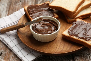 Tasty chocolate butter, slices of bread and knife on wooden table, closeup