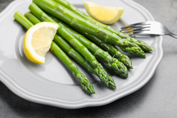 Tasty cooked asparagus served with lemon on grey table, closeup