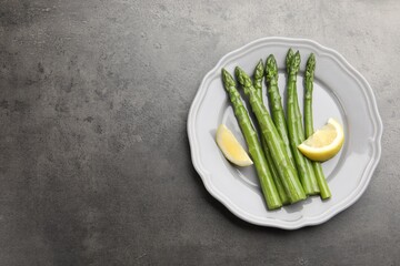 Tasty cooked asparagus served with lemon on grey table, top view. Space for text
