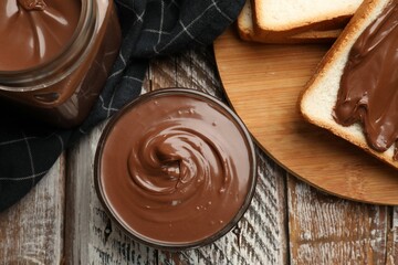 Tasty chocolate butter and slices of bread on wooden table, flat lay