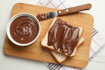 Tasty chocolate butter in bowl, slices of bread and knife on white marble table, top view