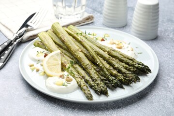 Tasty cooked asparagus served with lemon and sauce on grey table, closeup