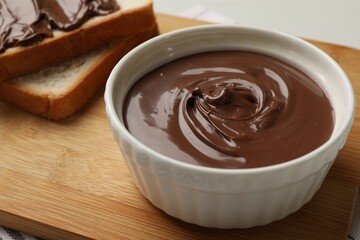 Tasty chocolate butter in bowl and slices of bread on table, closeup