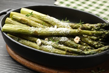 Tasty cooked asparagus served with parmesan on black wooden table, closeup
