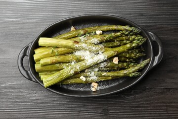 Tasty cooked asparagus served with parmesan on black wooden table, top view