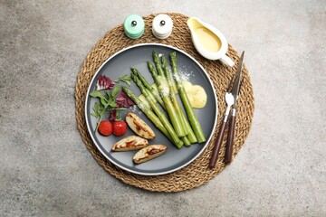 Tasty cooked asparagus served with baked potatoes, tomatoes and sauce on grey table, flat lay