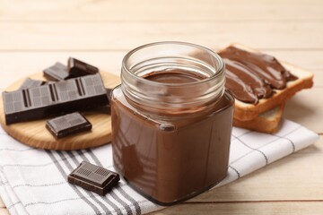 Tasty chocolate butter in glass jar, pieces and sandwiches on wooden table, closeup