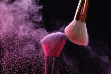 Makeup brushes with colorful eye shadows on black background, closeup