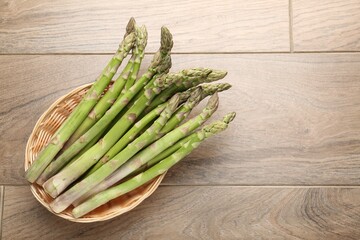 Fresh raw asparagus spears in wicker basket on wooden table, top view. Space for text