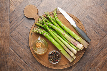 Fresh raw asparagus, spices, oil and knife on wooden table, top view