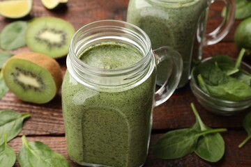 Tasty smoothie in mason jars, spinach leaves and kiwi on wooden table, closeup