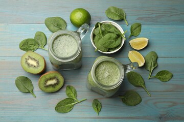 Tasty smoothie in mason jars, spinach leaves, kiwi and lime on light blue wooden table, flat lay
