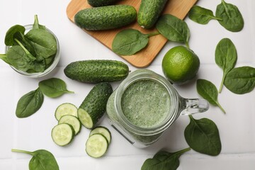 Tasty smoothie in mason jar, spinach leaves, lime and cucumber on white tiled table, flat lay