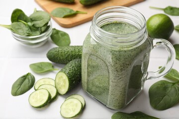 Tasty smoothie in mason jar, spinach leaves and cucumber on white table, closeup